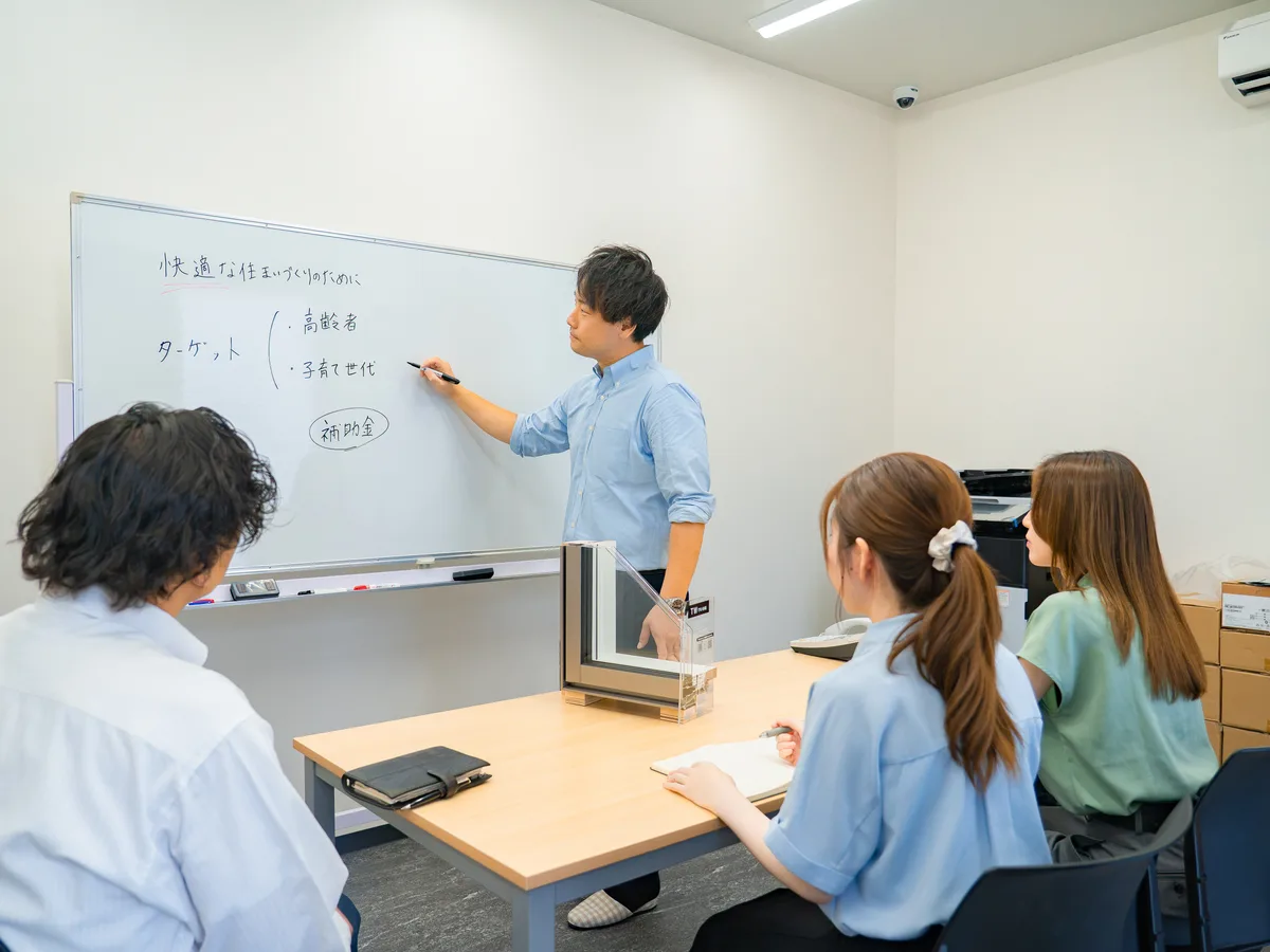 ホワイトボードの前で説明するスタッフと、着席して聴く3名の社内研修会